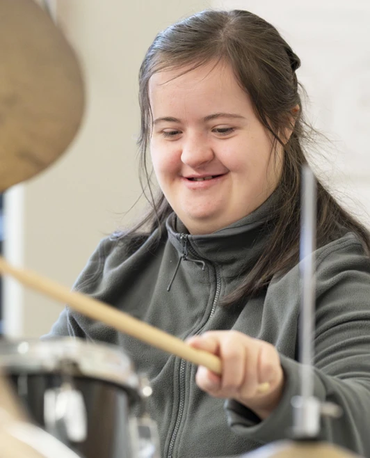 Young woman with Down syndrome smiling and playing the drums with enthusiasm during a music session. Young woman with Down syndrome smiling and playing the drums with enthusiasm during a music session.